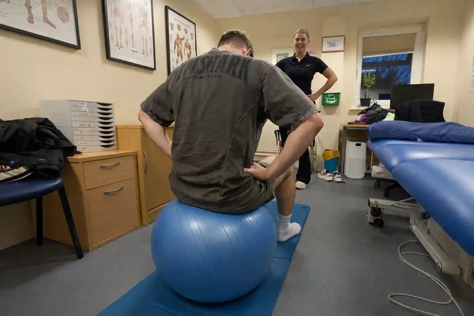 Physiotherapist supervising a patient doing a seated stability ball exercise for back rehabilitation at Phoenix Physio clinic